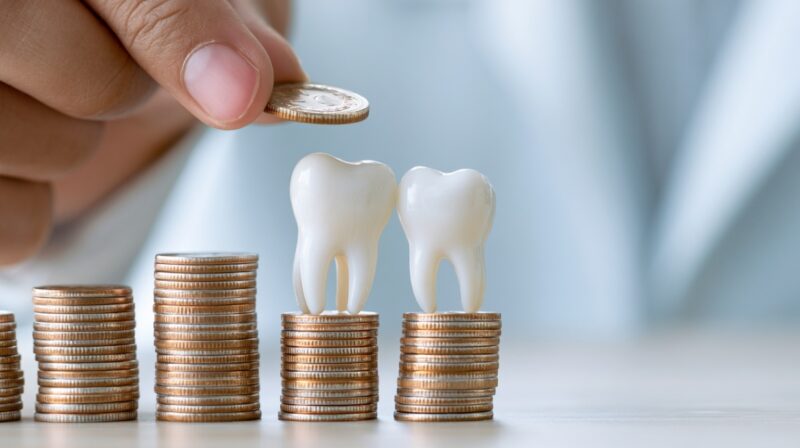 Two model teeth placed on stacks of coins while a hand holds another coin above them.
