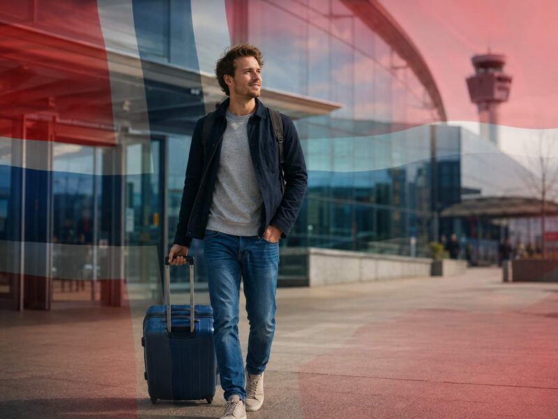 Man with luggage leaving an airport with a soft Norwegian flag overlay.